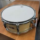 Světle žlutý buben s kovovými obručemi a mechanismy. Na blaně je viditelné logo značky Remo. Na korpusu je nalepený štítek s nápisem YAMAHA a dalšími…