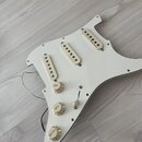 Bílý pickguard pro elektrickou kytaru s třemi krémovými snímači typu single-coil. Na středním a kobylkovém snímači je viditelný nápis "Nocdanima". So…