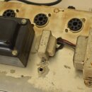 Fotografie zachycuje vnitřek elektronického zařízení s kovovým šasi. Jsou zde vidět tři vakuumové elektrony v paticích a tři transformátory různých v…