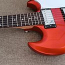 Detail elektrické kytary v oranžové metallic barvě s bílým pickguardem. Nástroj má hmatník z tmavého dřeva a dva snímače typu humbucker s chromovaným…