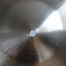 Detailní pohled na střed kovového činelu stříbrné barvy. Povrch vykazuje koncentrické rýhy z procesu výroby a odrazy světla. Na fotografii nejsou vid…
