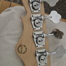 Záběr na hlavu basové kytary z přírodního světlého dřeva se čtyřmi chromovanými ladičkami. Na zadní straně hlavy je černý nápis „GGL GUITARS“, pod ní…