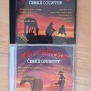 Dvě CD v plastových obalech s papírovými vložkami. Horní disk má nápis SBOHEM LÁSKO ČESKÉ COUNTRY, seznam skladek a v levém dolním rohu text Balíček…