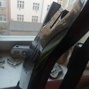 Detailní pohled na černý, lesklý povrch elektrického nástroje s výrazně hranatým a atypickým tvarem. Na povrchu jsou vidět odrazy okolí a drobné neči…