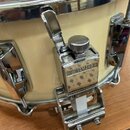 Detailní pohled na část světlého bubnu s chromovaným obručováním a mechanismem. Na kovovém mechanismu je viditelné logo a nápis YAMAHA. Povrch chromo…
