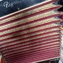 Detail akordeonu s černým povrchem a červenými měchy s křížovou texturou. Na horní části je bílý nápis Rigoletto. Povrch nástroje vykazuje známky opo…