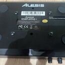 Zadní strana černého elektronického zařízení s nápisem ALESIS. Uprostřed je bílá nálepka s textem ALESIS SAMPLEPAD 4, označením (21)B51709187700164,…