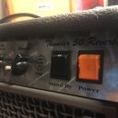 Detail kytarového komba s černým texturovaným potahem a kovovým předním panelem. Na panelu je nápis Thunder 50 Reverb a logo Tube Amp v kroužku. Jsou…