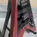 Detail elektrické kytary v červeném provedení s černým pickguardem. Na snímačích jsou viditelné nápisy "BUTY PICKUPS". Kytara je umístěna na černém s…