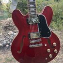 Červená polodubová elektrická kytara s černým pickguardem a dvěma humbuckery. Nástroj má chromovaný most a strunovník, čtyři ovládací knoflíky a dva…