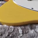 Detailní pohled na žluté tělo elektrické kytary s bílým pickguardem. Povrch laku je glossy, v dolní části těla je vidět drobné odřápání. Na fotce nej…