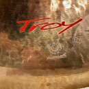 Detailní záběr na povrch mosazného činele s viditelným kovaným zpracováním. Na povrchu je červený nápis "Troy" a níže kulaté logo s nápisem "MADE IN…