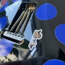 Detail korpusu černé elektrické kytary s modrými kruhovými nálepkami. Je vidět kovový kobylník s pružinami a dvě menší nálepky s motivem andělíčků. P…