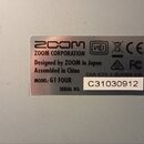 Fotografie detailně zachycuje stříbrný informační štítek na povrchu zařízení. Štítek obsahuje logo ZOOM, nápis ZOOM CORPORATION a text Designed by ZO…