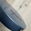 Detail spodní části modrého trupu elektrického nástroje s matným povrchem. Na zadní straně je vidět podélný otvor pro přístup k elektronice, upevněný…