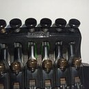 Detailní pohled na černý kytarový kobylník z kovu. Na horní hraně je vidět nápis SCHALLER. Povrch vykazuje známky používání a mírné opotřebení, zejmé…
