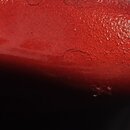 Detailní záběr na červený lakovaný povrch hudebního nástroje. Povrch má zrnitou texturu a jsou na něm vidět drobné škrábance a oděrky, které jsou v o…