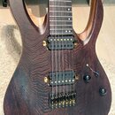 Elektrická kytara s tmavě hnědým dřevěným povrchem a výraznou strukturou zrna. Nástroj má dva humbuckery s černými snímači a zlatým hardwarem, včetně…