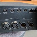 Zadní panel černého elektronického zařízení s kovovým šasi a ventilačními otvory. V horní části jsou čtyři přepínače s popisky INPUT GROUND LIFT, OPT…