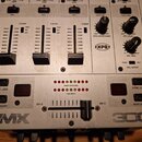 Stříbrný DJ mixér s ovládacími prvky, včetně faderů a otočných knoflíků. Na panelu jsou viditelné nápisy VMX a 300, logo XPO a označení kanálů CH 2 a…