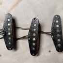 Tři elektrické snímače s černými plastovými kryty a viditelnými magnety. Snímače jsou propojené mezi sebou vodiči a mají viditelné stopy opotřebení a…