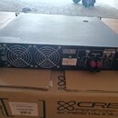 Černý výkonový zesilovač v kovovém šasi s dvěma velkými ventilátory na zadním panelu. Na přístroji je bílý nápis WWW.CRESTAUDIO.COM a logo CREST AUDI…