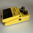 Žlutý efekt pedál s černým spínacím tlačítkem a třemi černými ovládacími knoflíky. Na horní straně jsou nápisy SUPER OverDrive SD-1, OUTPUT, INPUT, L…
