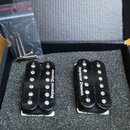 V černé krabičce s pěnovou výplní jsou dva černé humbuckery. Oba mají bílý nápis Seymour Duncan. Vedle nich je v průhledném plastovém sáčku sada mont…