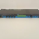 Černý rackový procesor s modrým předním panelem a LCD displejem. Na panelu je nápis MPX 500 24-Bit Dual Channel Processor a vpravo logo lexicon. Zaří…