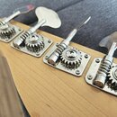 Detail hlavy basové kytary z přírodního dřeva se čtyřmi chromovanými ladicími mechanismy. Na základních deskách dvou pravých mechanismů je vyražen ná…