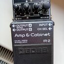 Černý efekt pedál značky BOSS s nápisem Amp & Cabinet a označením modelu IR-2. Horní část obsahuje čtyři ovládací knoflíky a nápisy CHECK, BASS, MIDD…