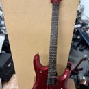 Tmavě červená elektrická kytara s kovovými strunami a hnedým hmatníkem. Na hlavě je svisle napsaný bílý nápis MUSIC MAN. Kytara má dva humbuckery, je…