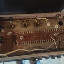 Fotografie zachycuje vnitřek elektronického zařízení, pravděpodobně zesilovače nebo efektu. Je vidět hnědý základ s řadou zapájených součástek, někol…