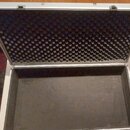 Otevřený hliníkový kufřík s vnitřním polstrováním. Víko je vyloženo černou akustickou pěnou s pyramidovitým profilem, dno je potaženo hladkým černým…