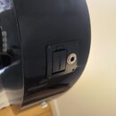 Detail černé lakované desky hudebního nástroje s osazeným vstupem pro jack kabel. Vedle konektoru je umístěn černý plastový kryt s nápisem FISHMAN. C…