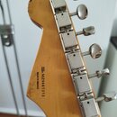 Zadní strana hlavy kytary z přírodního dřeva s lakovaným povrchem. Na dřevě je černý nápis MADE IN MEXICO a SERIAL NUMBER MZ9441313. Na hlavě jsou na…