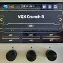 Fotografie zachycuje displej digitálního zařízení s třemi černými ovládacími knoflíky pod ním. Na obrazovce je bílý nápis VOX Crunch R a pod ním kód…