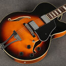 Polodupatá elektrická kytara s oranžovo-černým sunburst povrchem a černým pickguardem. Nástroj má dva humbuckery, čtyři černé oválné knofíky a chromo…
