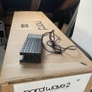 Černý sustain pedál značky Roland s nápisem RV-10. Pedál leží na hnědé cardboardové krabici s nápisem nord a štítkem, na kterém je uvedeno nord wave…