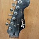 Fotografie zachycuje hlavu elektrické kytary v tmavě šedé barvě s metalickým efektem. Na hlavě jsou vidět nápisy Squier® STRATOCASTER® a logo Fender.…