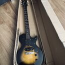 Elektrická kytara s trupem v černo-žlutém přechodovém odstínu (sunburst) a černým hmatníkem. Na hlavě je viditelné logo Vintage. Nástroj má jeden sní…