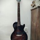 Elektrická kytara s tmavě hnědým gradientem (sunburst) a černým hmatníkem. Na hlavě je bílý nápis Epiphone. Nástroj má dva humbuckery, jeden tónový a…