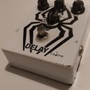 Bílý efekt pedál s černým grafickým motivem pavouka. Na horní straně jsou tři černé ovládací knoflíky s popisky TIME, RATE a MIX, doprovázené přepína…