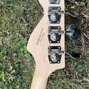 Zadní strana hlavy basové kytary z přírodního světlého dřeva. Na zadní straně jsou čtyři chromované ladičky a nápisy „Crafted in China“ a „S/N:CYB181…