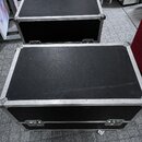 Dvě černé transportní bedny s hliníkovými hranami a kovovými rohy. Bedny mají povrch z černého texturovaného materiálu a jsou vybaveny kovovými zámky…