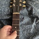 Fotografie zachycuje hmatník a hlavu elektrické kytary černé barvy. Na hlavě je bílý nápis Gibson a šest ladících kol s krémovými knoflíky. Hmatník j…