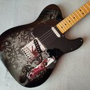 Černá elektrická kytara typu Telecaster se světlým javorovým hmatníkem. Tělo je zdobeno šedým ornamentálním vzorem paisley. Nástroj má černý pickguar…