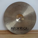 Kovový činel zlatavé barvy s viditelným broušením povrchu. V dolní části je černý nápis „istanbul Agop Handmade cymbals from Turkey“. V horní části j…