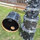 Sada bubnů s černým mramorovaným povrchem a chromovaným kováním. Na vnitřní straně největšího bubnu je bílé logo drums dw. Na ostatních bubnech jsou…