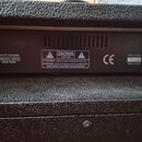 Fotografie zachycuje zadní část černého hudebního zesilovače s texturovaným povrchem. Na černém štítku je nápis INPUT POWER 230VAC-50Hz 80W MAX, varo…